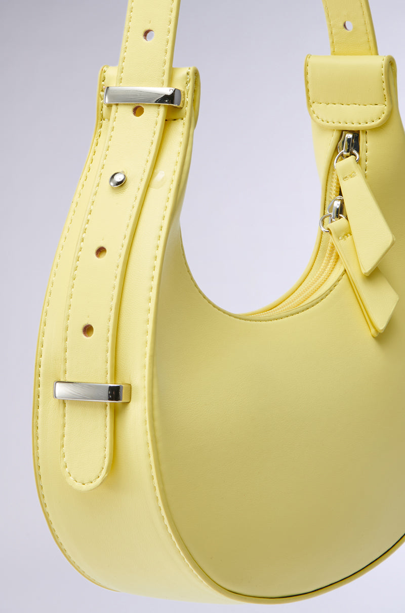 Close-up of the GET WITH THE TREND PU PURSE in light yellow faux leather, featuring silver buckles, a crescent shape, and a small attached pouch, set against a plain gray background.