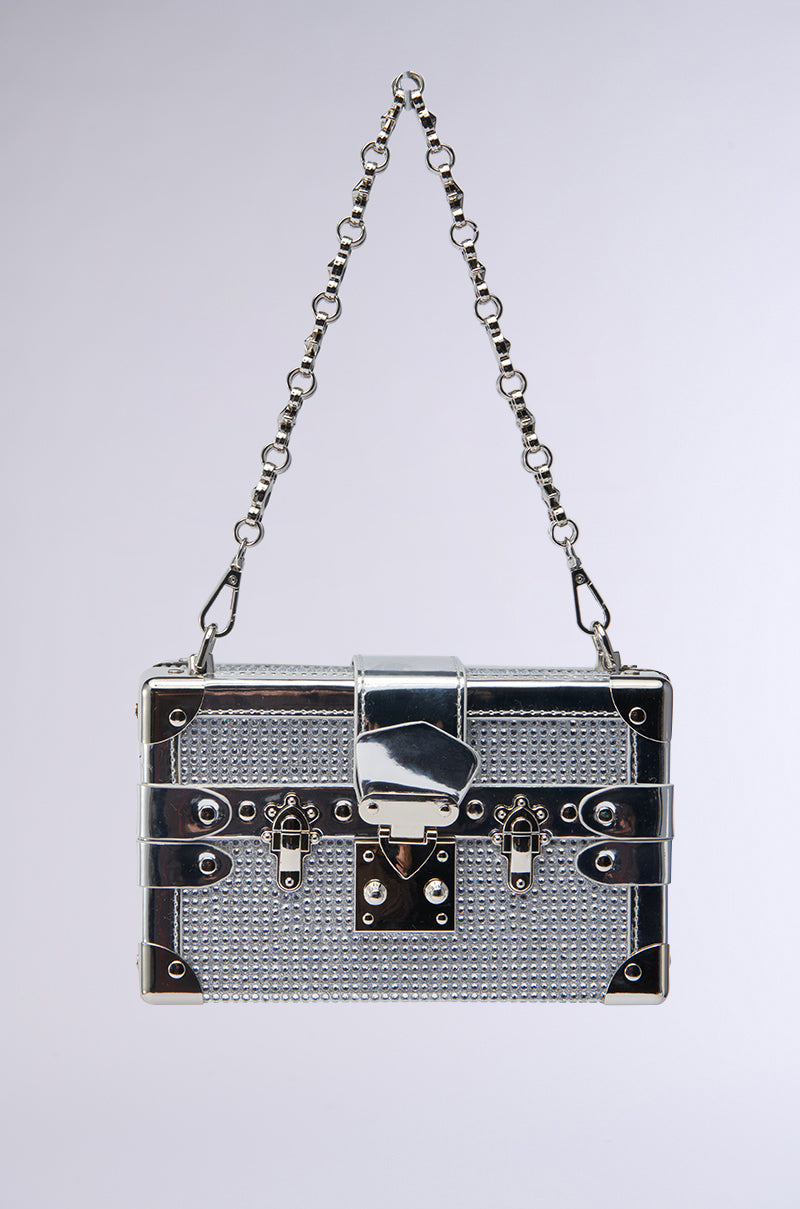 The LOU BLING TRUNK BAG is a small, metallic silver purse with a textured surface, front latch closure, and chain strap, shown on a plain light gray background—ideal as a statement piece for any occasion.