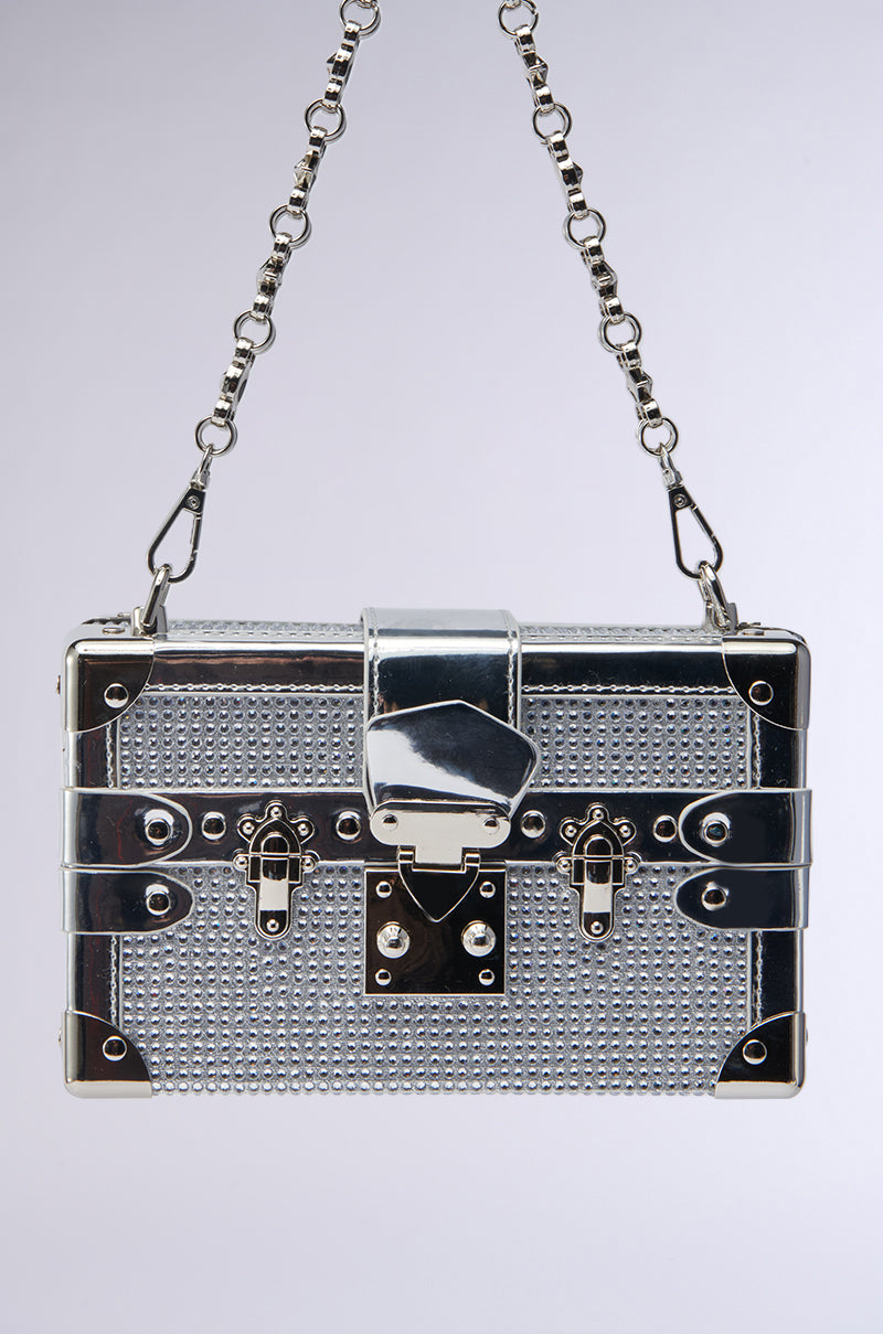 The LOU BLING TRUNK BAG is a small, rectangular metallic silver purse with a textured surface, chain strap, and detailed clasp—its sparkling design resembles a miniature treasure chest.