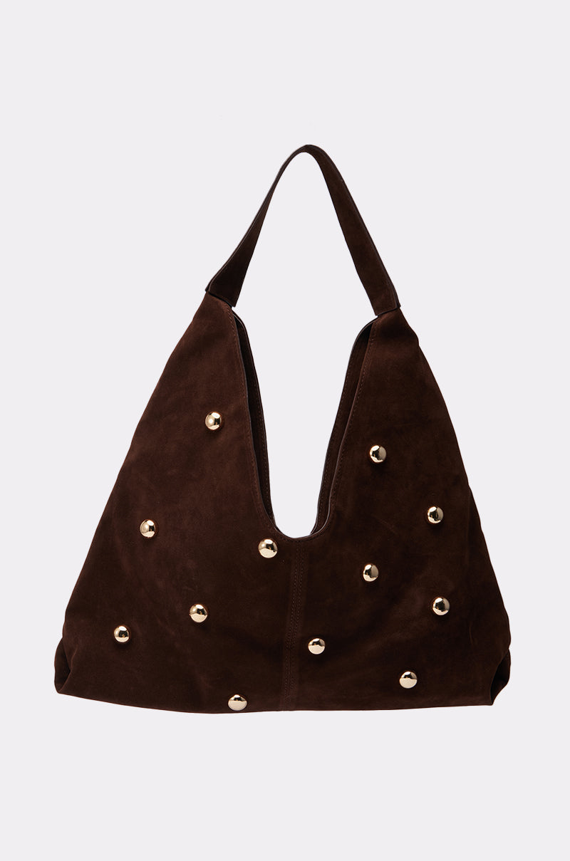 The TAYLOR SUEDE BALL TOTE is a dark brown suede tote with a wide handle, deep V-shaped opening, and evenly spaced round gold studs, shown against a plain light gray background.