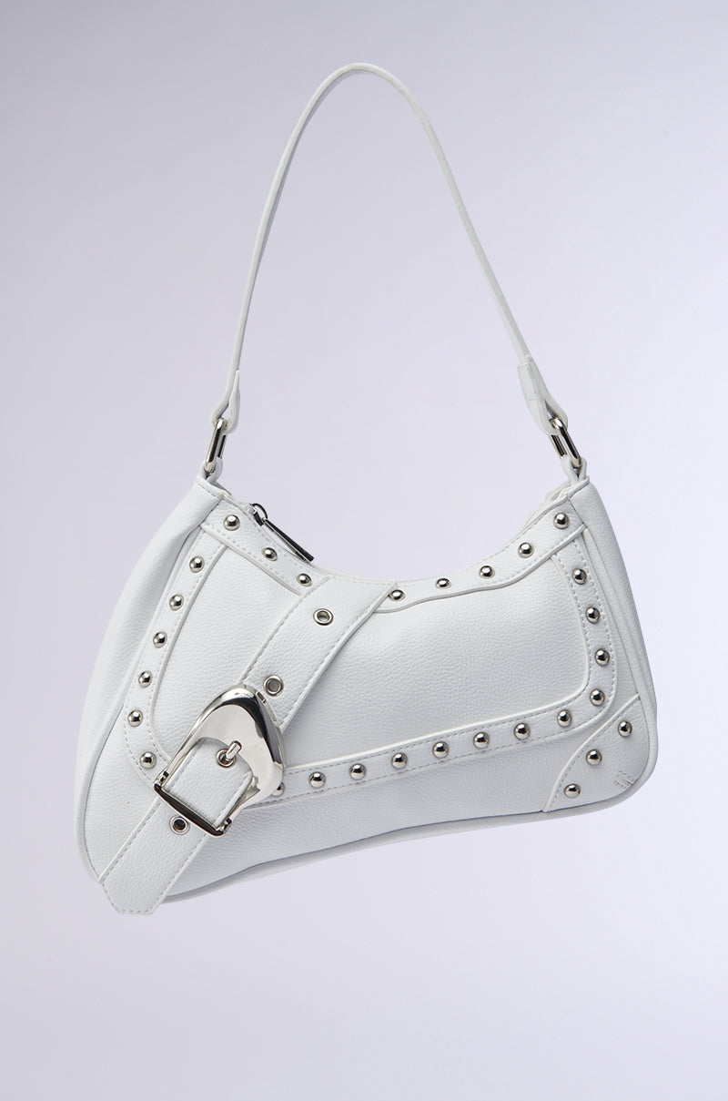 The BELLA PURSE is a white faux leather shoulder bag with silver studs, a decorative strap featuring an oversized buckle, and a curved modern design, pictured on a plain light gray background. 0