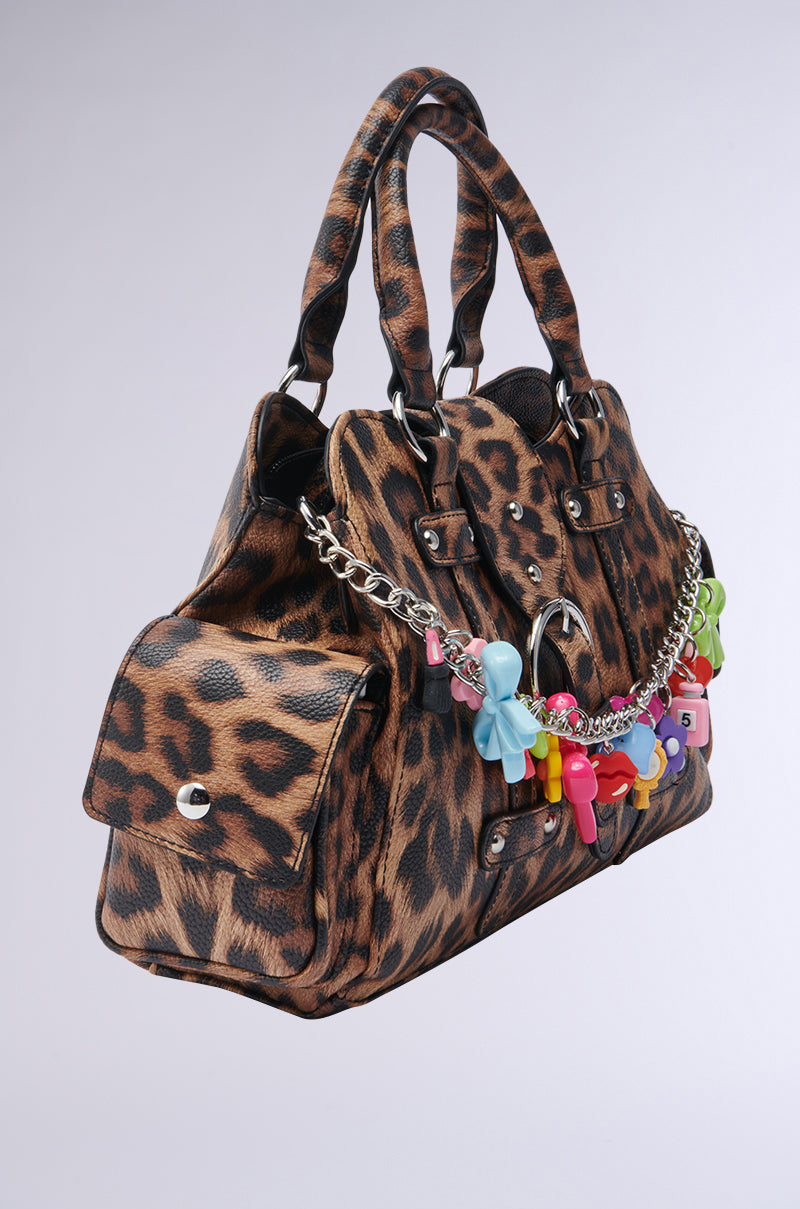 The ITS BETTER WILD PURSE features a cheetah print, double handles, side pocket, and a silver chain adorned with colorful Y2K-style keychains. It's displayed against a plain light gray background. 3
