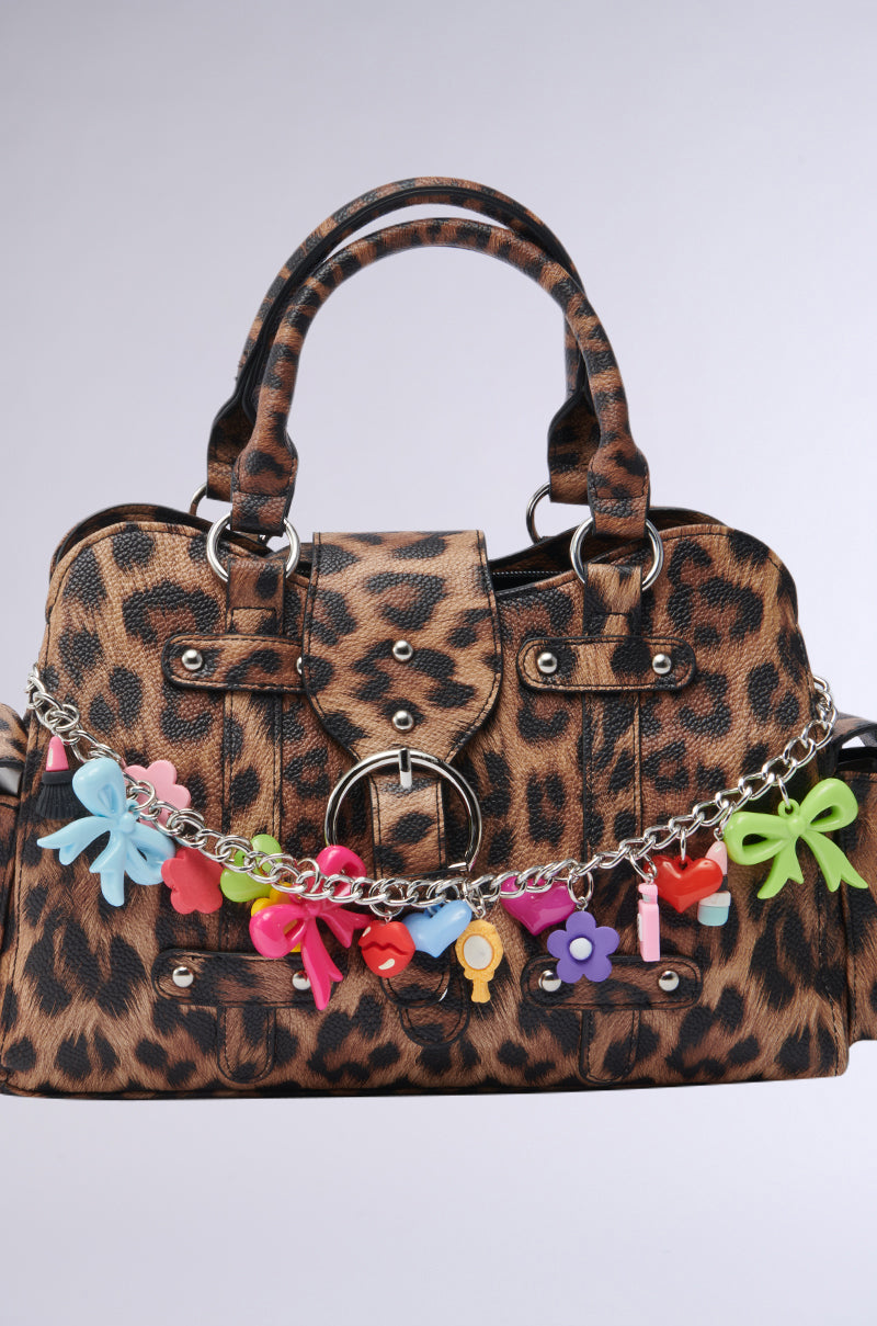 The ITS BETTER WILD PURSE features a cheetah print, double handles, a silver chain, and playful Y2K-style accents like colorful bows, keys, and flowers draped across the front. 4