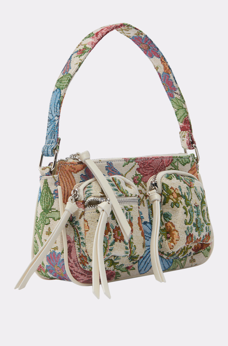 THE REAL KNOW PURSE by AKIRA Label: a small shoulder bag with a floral tapestry design, short handle, two front zippered pockets with white pulls, and a colorful green, blue, pink, and beige pattern on a light background. 2