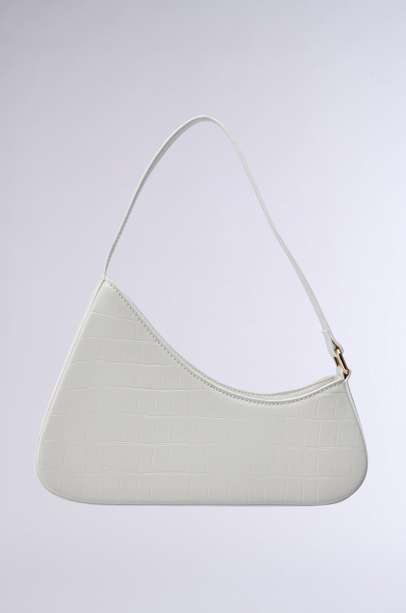 The CRY ABOUT IT PURSE is a minimalist off-white, crocodile-embossed faux leather handbag with an asymmetrical shape, chic shoulder bag design, and a single thin strap, shown against a light gray background.