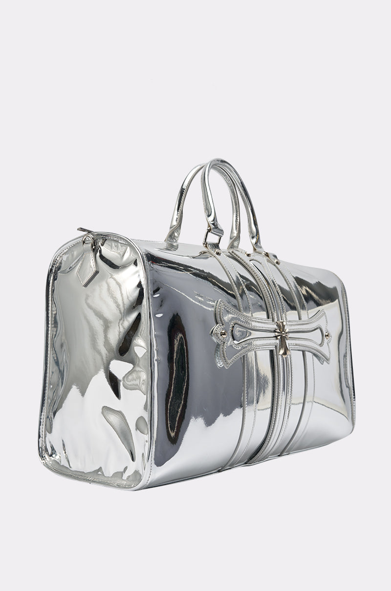 The IM CHROME DUFFEL, a shiny metallic silver oversized gym bag with double handles and a side zipper pocket, is shown against a plain light background—perfect for travel or daily use.