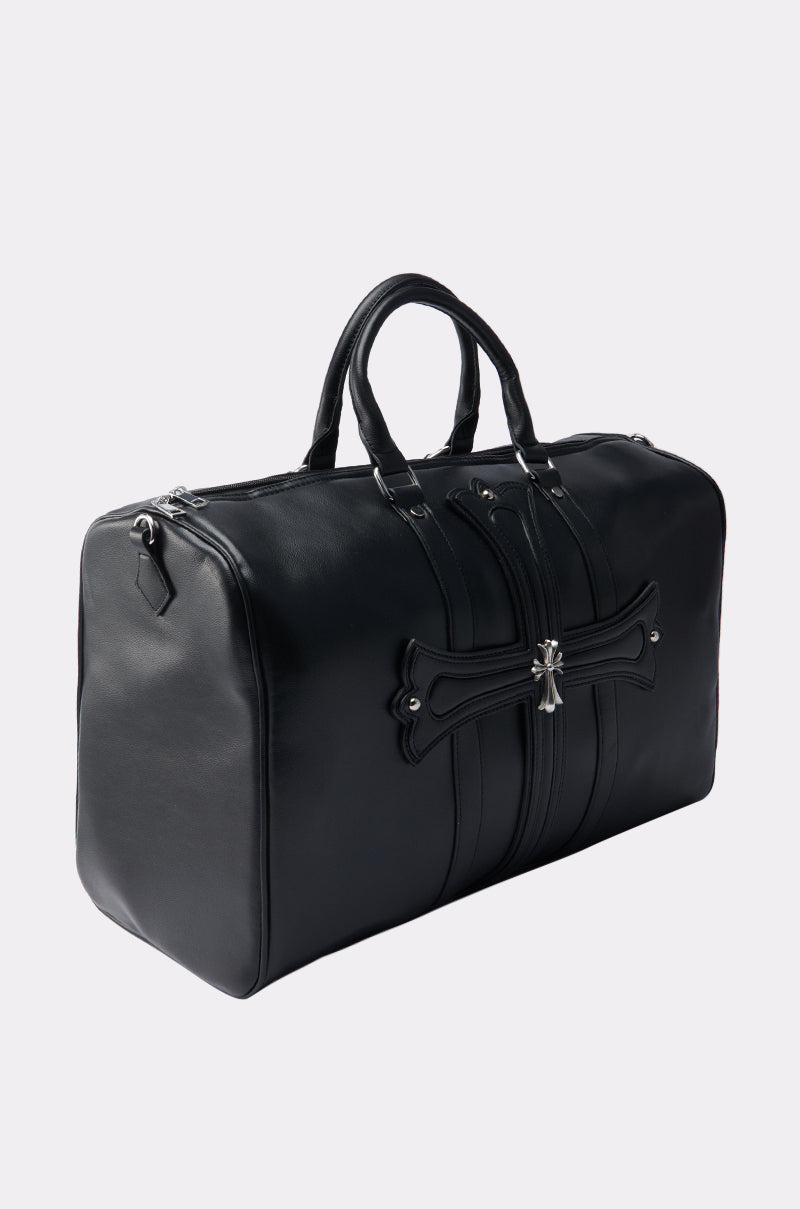 The EVERYTHING CHROME DUFFEL BAG is a black faux leather duffel featuring dual handles, silver zippers, stud hardware, and a cross-shaped accent on the front. Displayed against a plain light gray background.