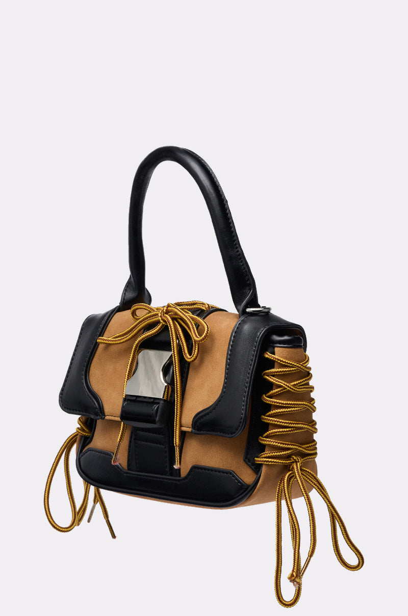 The IN THE STREETS PURSE features a tan suede body, black faux leather handles and trim, gold lace-up sides, a large metallic front clasp, and decorative gold cord accents for a stylish, elegant look. 3