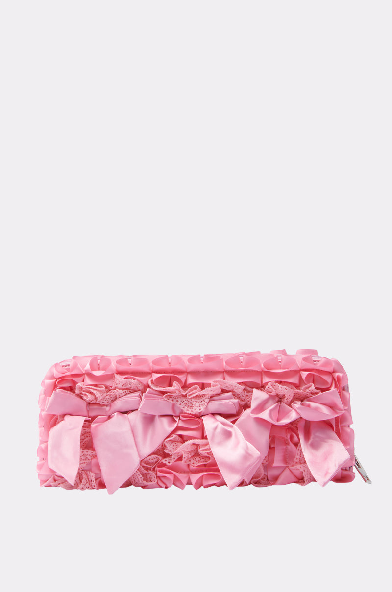 The WITH A BOW CLUTCH is a structured rectangular pink satin bag, featuring oversized satin bows and delicate lace detailing, displayed on a plain light background.