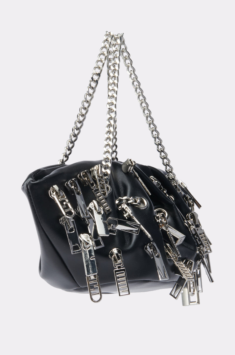 The ZIP IT CHARM PURSE is a black faux leather bag featuring big silver zipper pulls and bold chain handles, making it the ultimate statement accessory for street-style looks.