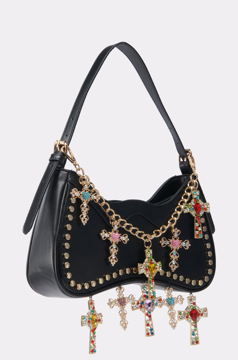 The SO DOLCE CROSS PURSE is a black faux leather handbag with gold studs, a decorative gold chain featuring jeweled cross pendants on the front and bottom, and a roomy interior for your essentials. 1
