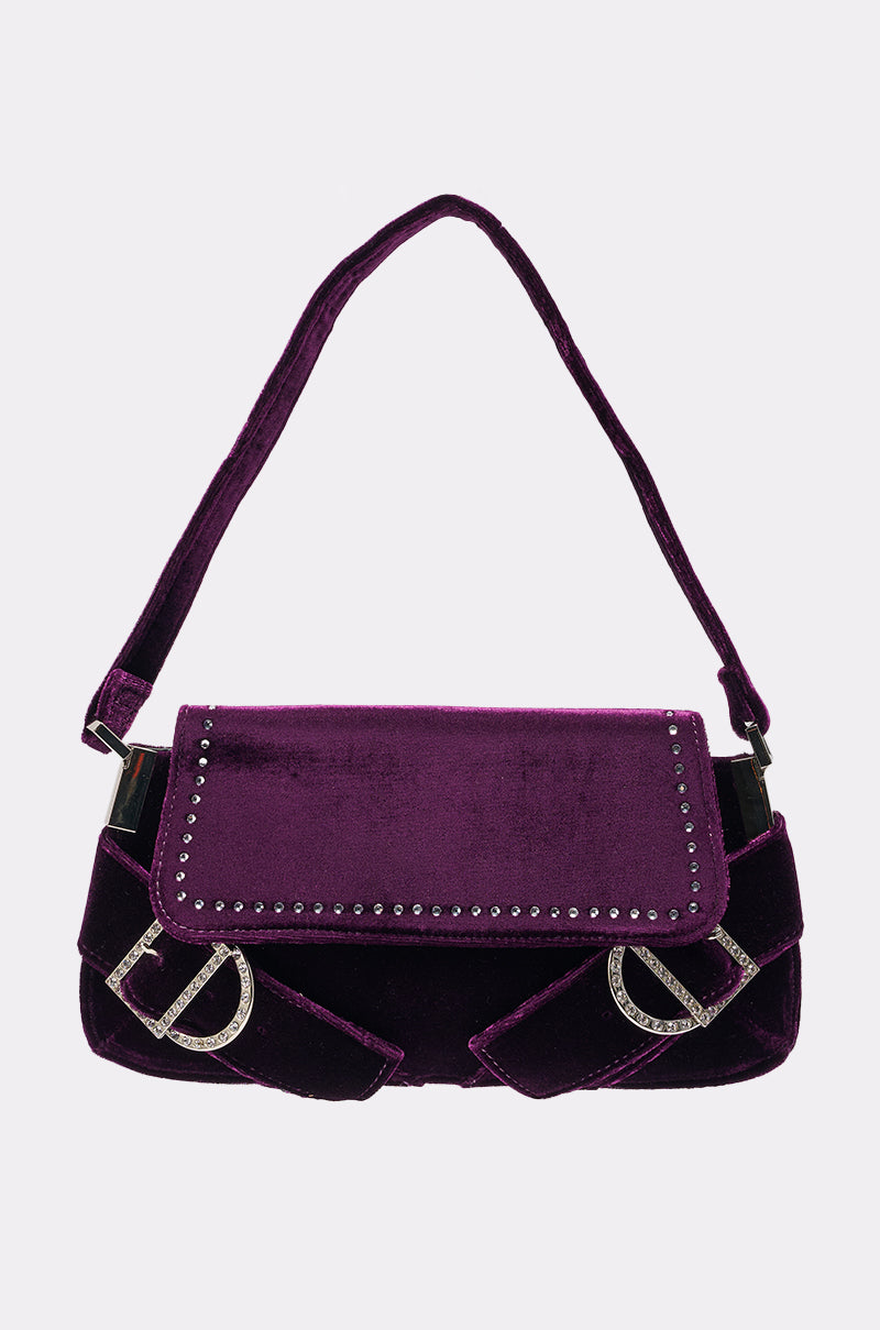 The LEILA VELVET PURSE is a dark purple velvet baguette handbag with a single strap, silver studs on the flap, and two silver "D" accents on the front corners. 0