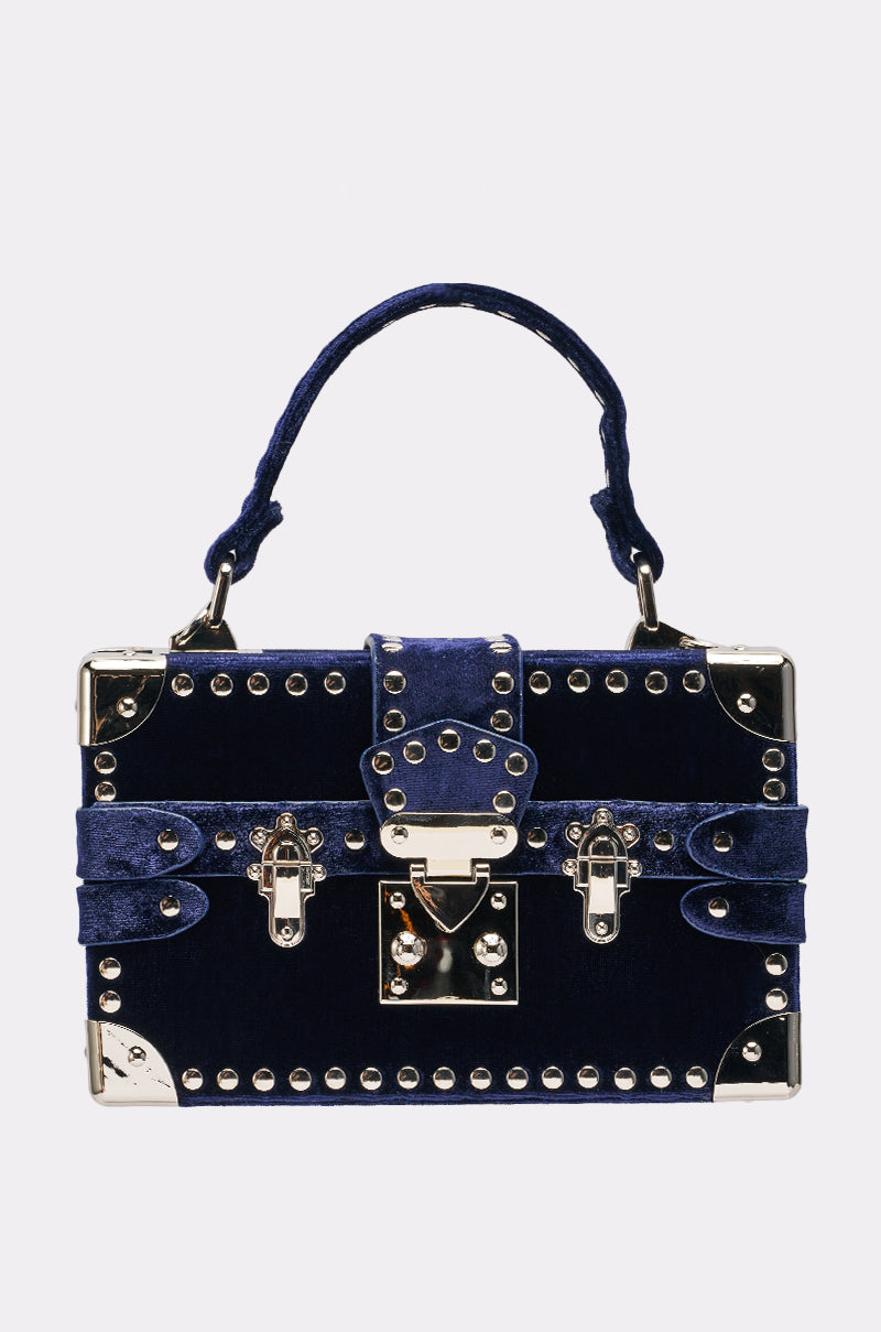 Introducing the TRUNK SHOW PURSE: a dark blue velvet evening bag inspired by vintage trunks, with silver studs, metal corners, a top handle, and decorative front buckle and latch details.