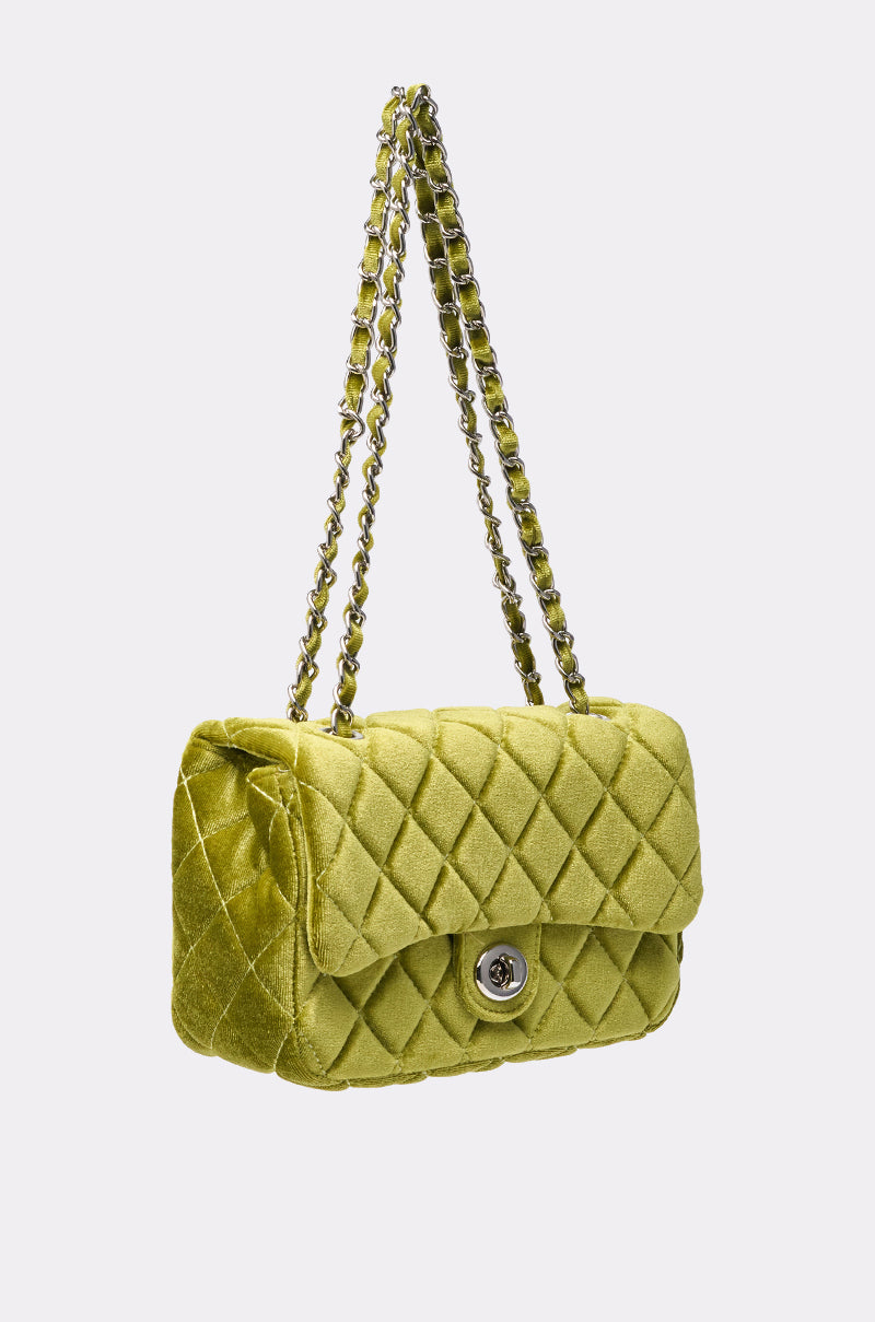 The NIKKI VELVET QUILTED PURSE features chartreuse quilted velvet, a flap with silver turn-lock clasp, and a double chain strap woven with matching fabric for a plush, elegant look. 2