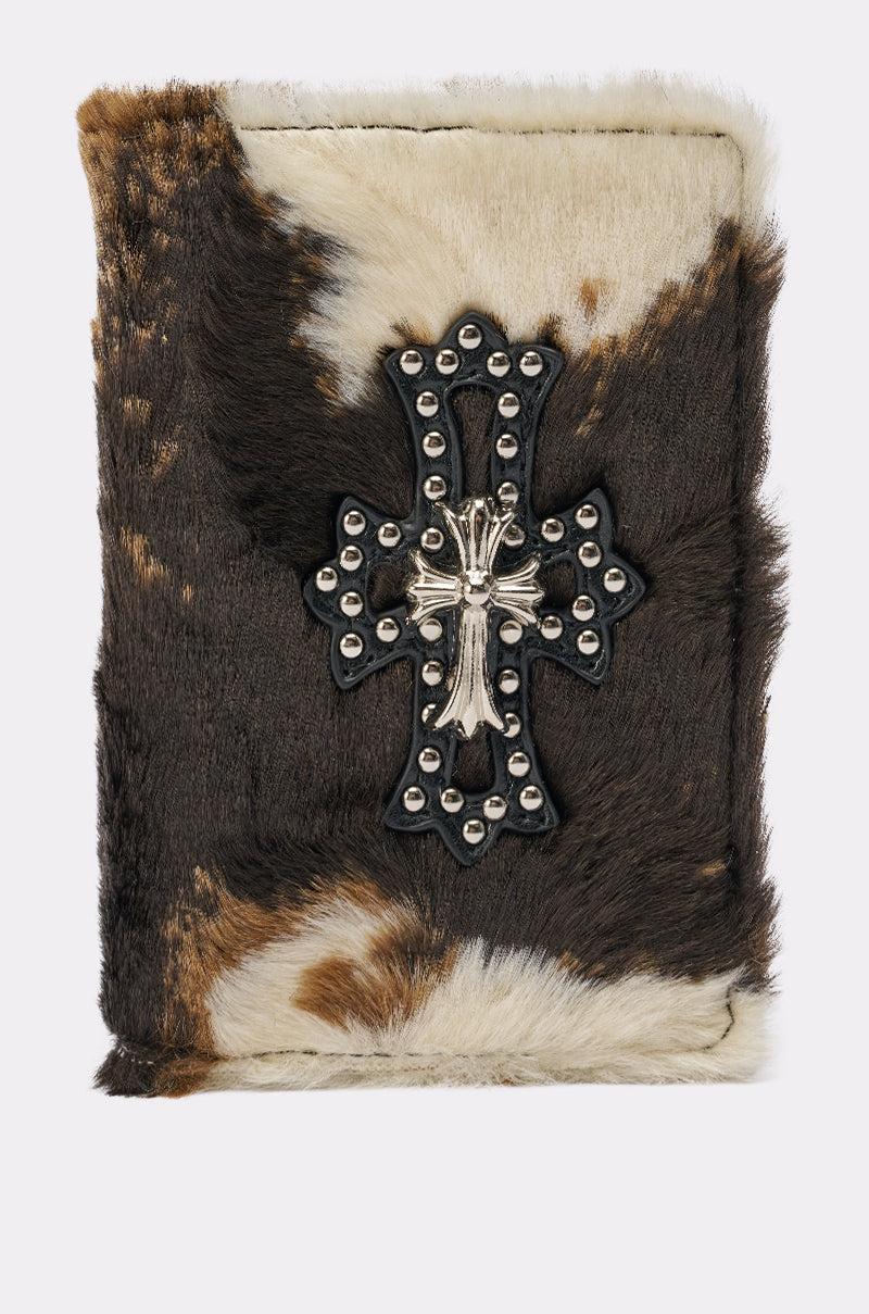 The HIGH STANDARDS FAUX FUR PASSPORT COVER, featuring a cow print, black and silver cross emblem, and metal studs, is a unique addition to your travel essentials. 1