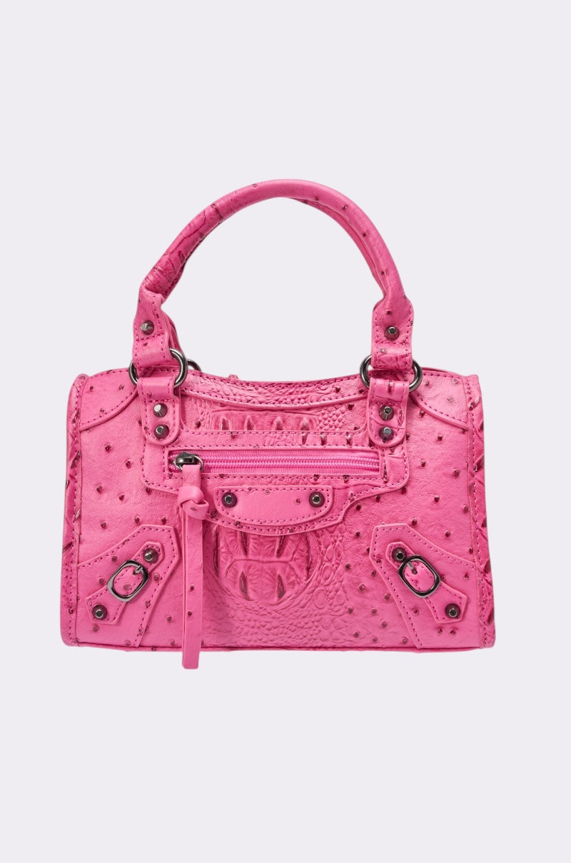 The ON MY NERVES PURSE is a small, bright pink faux leather structured handbag featuring an ostrich-like texture, top handles, silver hardware, a zippered front pocket, and decorative buckled accents.