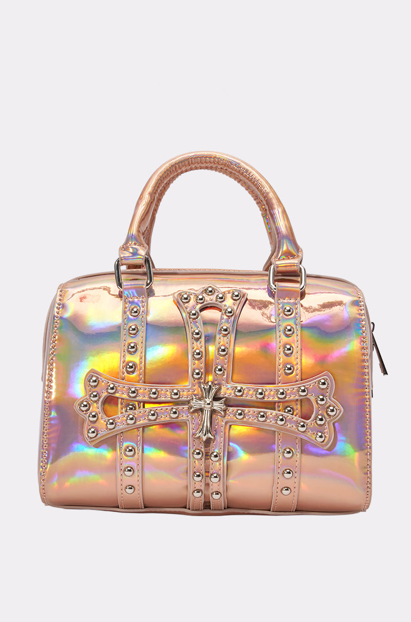 The FEELIN ROSIE MINI BOWLING BAG is a shiny, iridescent metallic rose gold bag with double handles, featuring a large metal studded cross design on the front and a side zipper closure.
