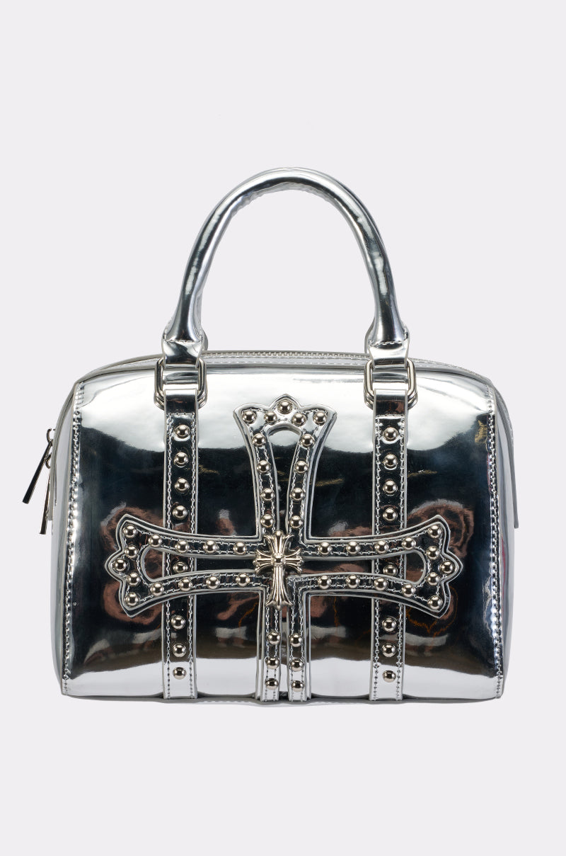 The MINI BOWLING BAG is a shiny metallic silver faux leather accessory featuring double handles and a mini bowling bag silhouette, accented on the front with an ornate studded cross and additional stud detailing.