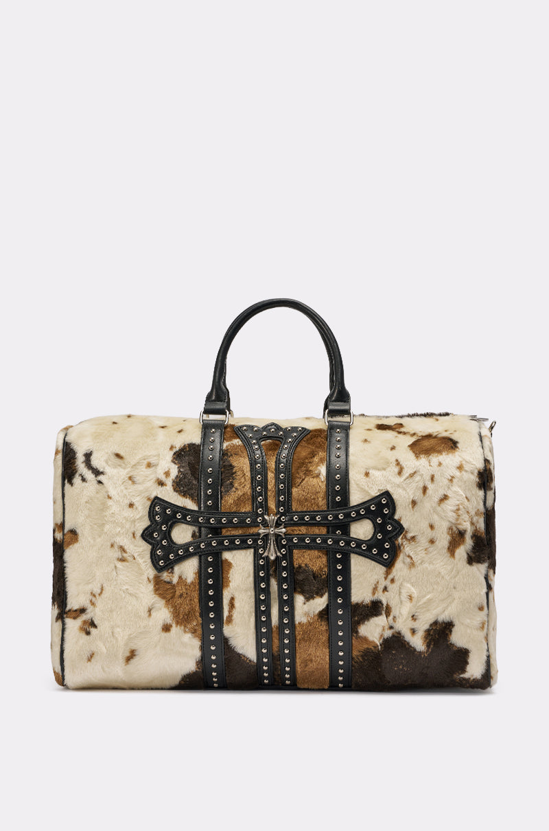The HIGH STANDARDS FAUX FUR DUFFEL is a spacious western-style travel bag with black leather handles, studded accents, and a patterned cowhide exterior in brown, white, and black. 1