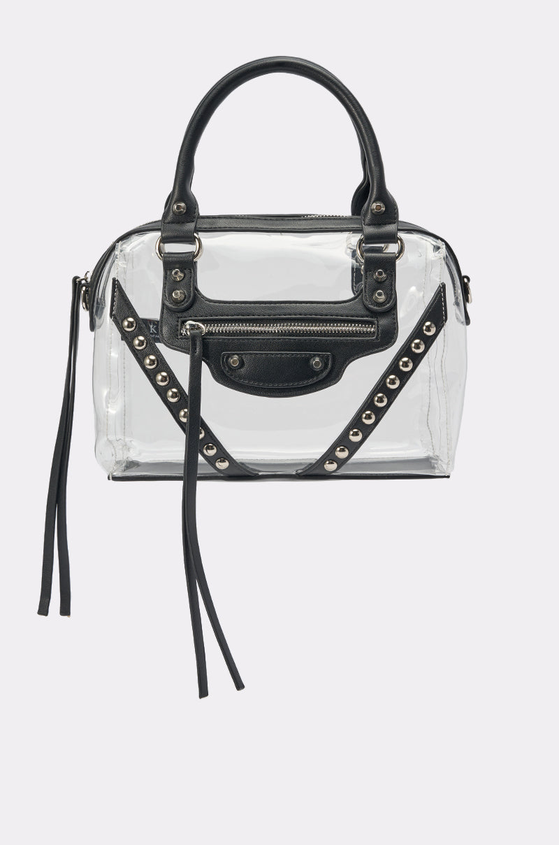 The IT GIRL CLEAR PURSE is a clear, rectangular stadium-approved bag featuring black leather trim, double handles, silver studs, zipper accents, and decorative front straps. 0