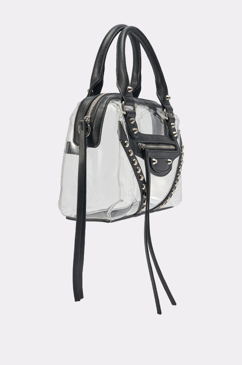 The IT GIRL CLEAR PURSE is a box-shaped clear bag with black leather handles, trim, and silver studs. With long black tassels and zipper details, this stadium approved purse is ideal for concerts or festivals. 2