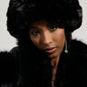 A woman wearing the LUXE JENNY FAUX FUR HEADBAND in black exudes cozy chic style as she gazes directly at the camera. Her long earrings enhance her winter accessory, while her neutral expression stands out against a simple backdrop.