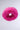 A circular piece of plush faux fur with a soft, feather-like texture is suspended against a plain white background, resembling the SABRINA FAUX FUR HEADBAND in vibrant hot pink.