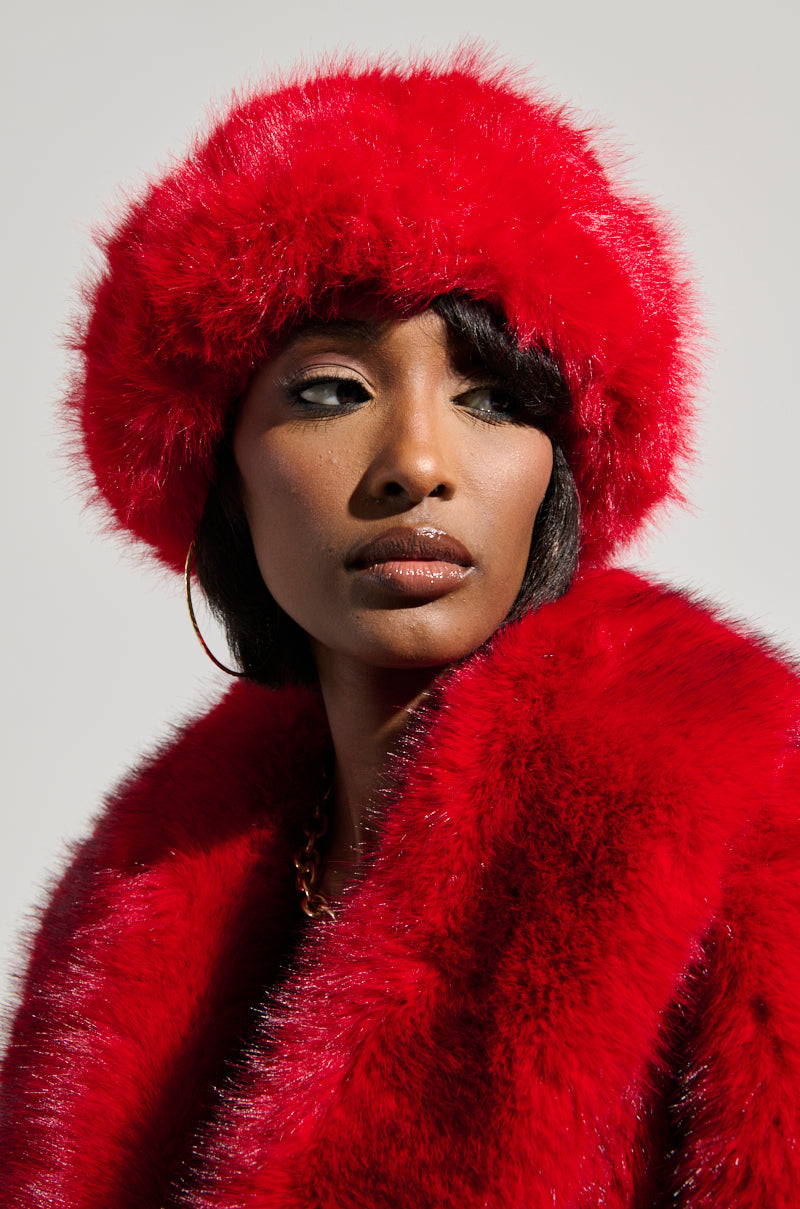 Wearing a coordinated red fur coat and the LOOK AT ME NOW FAUX FUR HEADBAND, a person gazes off to the side. The soft, neutral gray background accentuates their vibrant red ensemble. The faux fur headband complements their serene expression and expertly applied makeup, enhancing the overall elegance of their appearance. 0