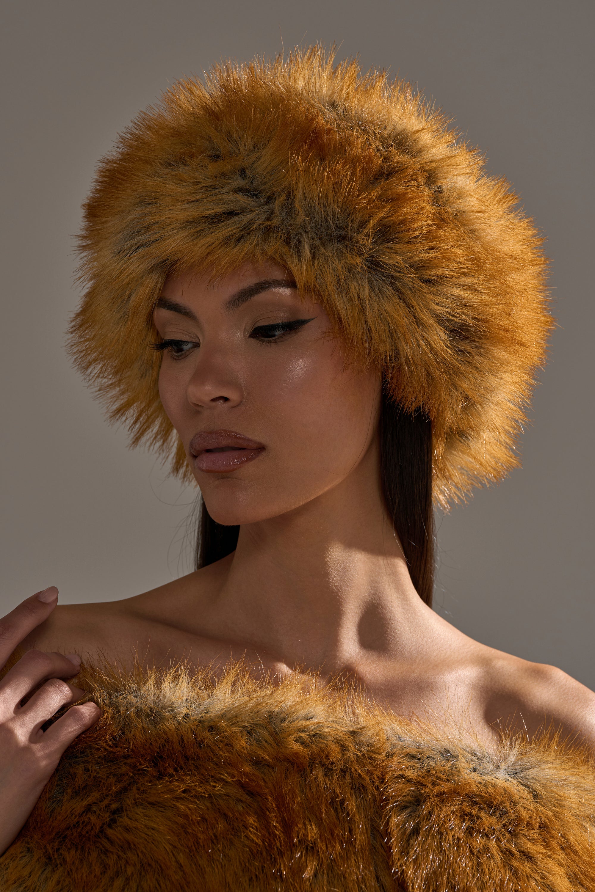 A woman wears the REALLY LIKE THAT FAUX FUR HEADBAND in orange-brown, gazing down calmly against a neutral backdrop to showcase this chic, cozy cold-weather accessory. 0