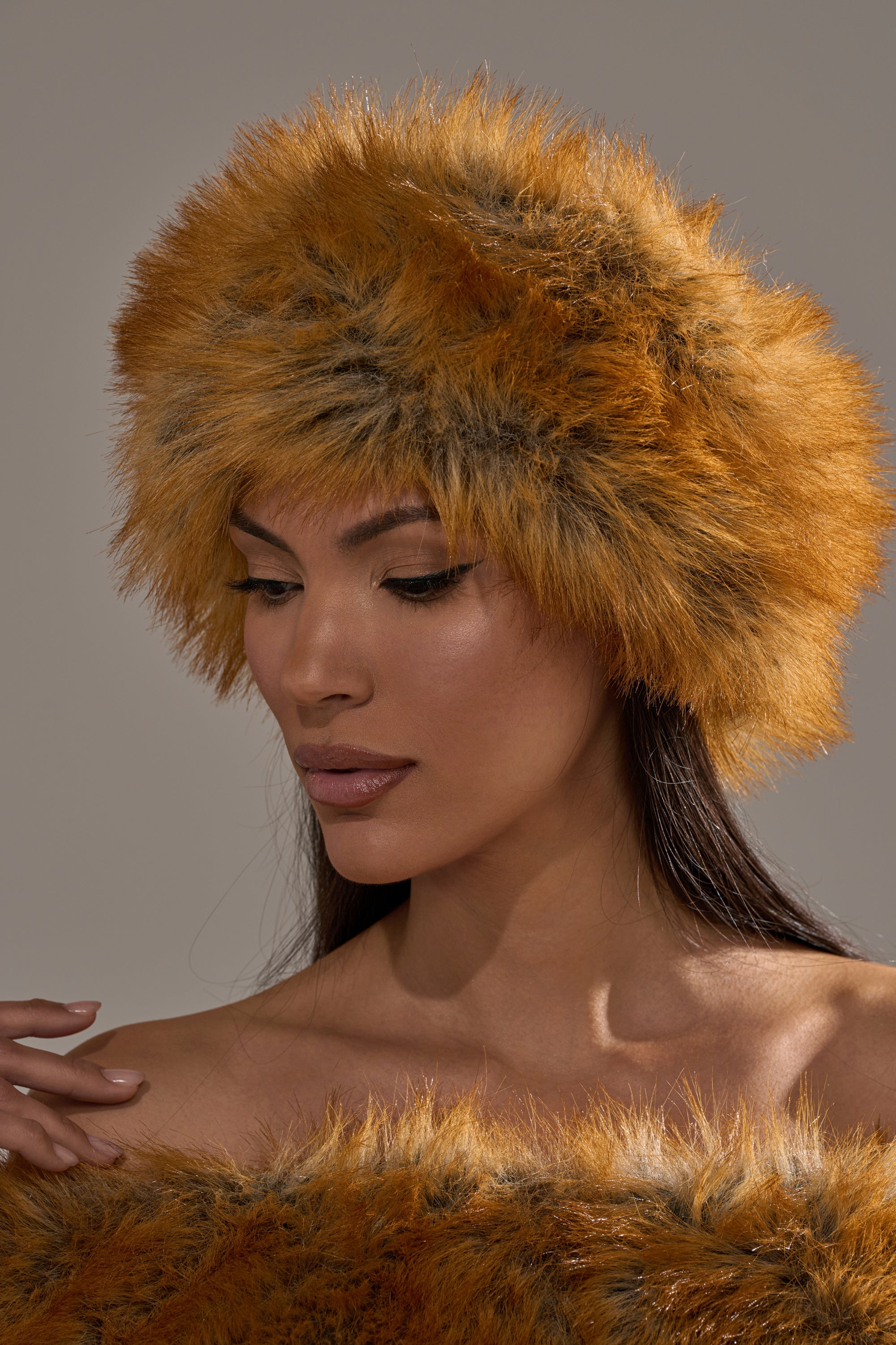 A woman wears the REALLY LIKE THAT FAUX FUR HEADBAND in orange-brown, along with a matching garment, looking down with a neutral expression against a plain background—an elegant cold-weather accessory. 1