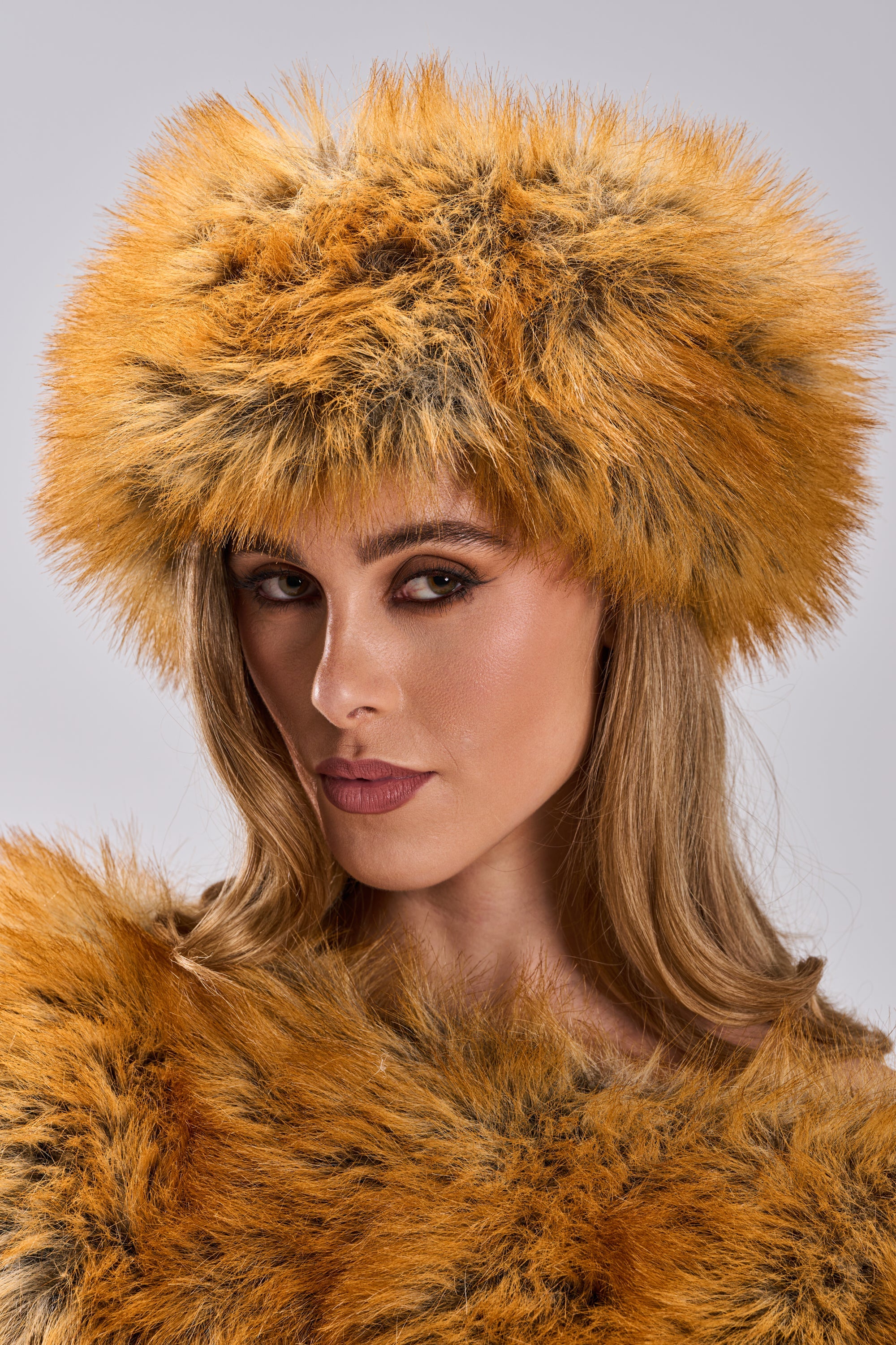 A woman with long blonde hair wears the REALLY LIKE THAT FAUX FUR HEADBAND in orange and brown faux fox fur, confidently facing the camera against a neutral gray backdrop—a standout cold-weather accessory. 4