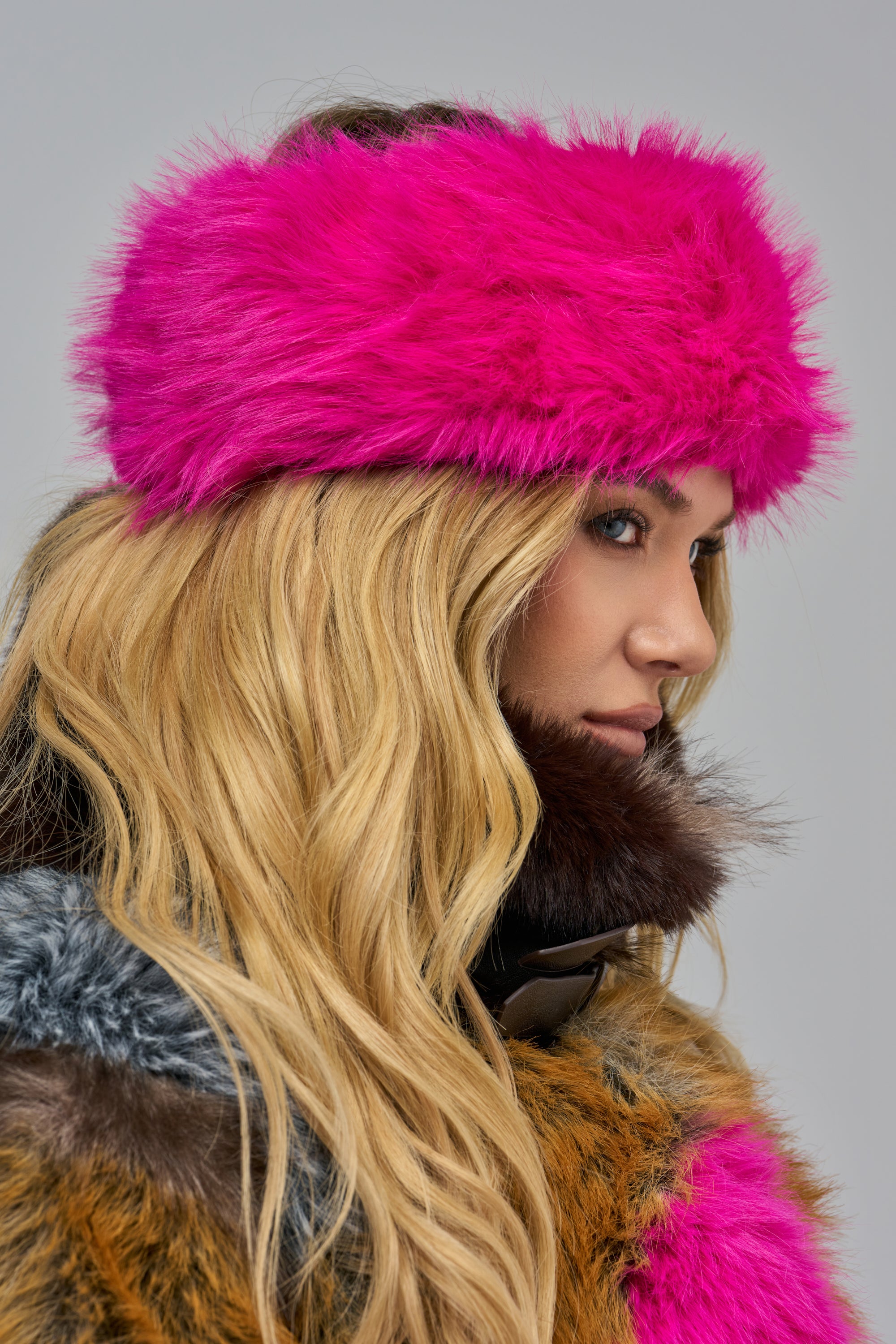 A person with long blonde hair wears a hot pink THATS HOT FAUX FUR HEADBAND, a vibrant accessory for winter streetwear.