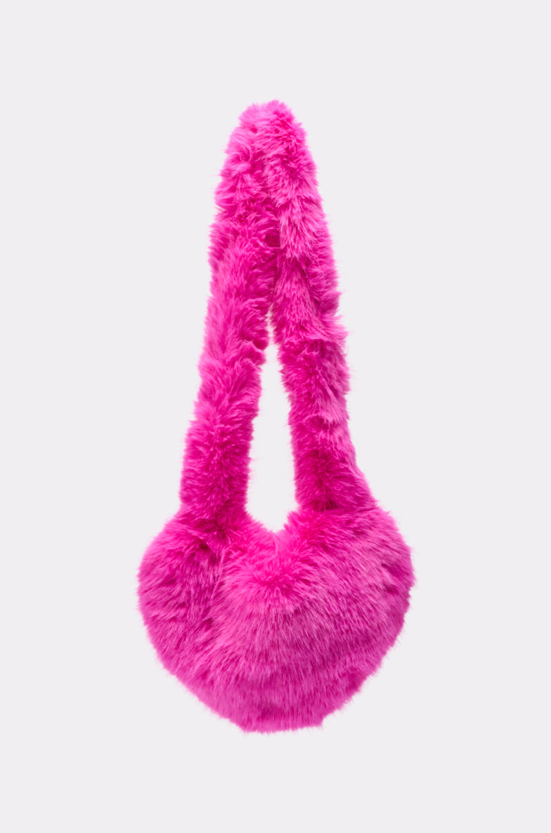 The LANA FAUX FUR HEART BAG IN PINK is a bright pink plush shoulder bag with a soft, fluffy finish, a rounded bottom, and a thick strap, displayed against a plain light gray background. 3