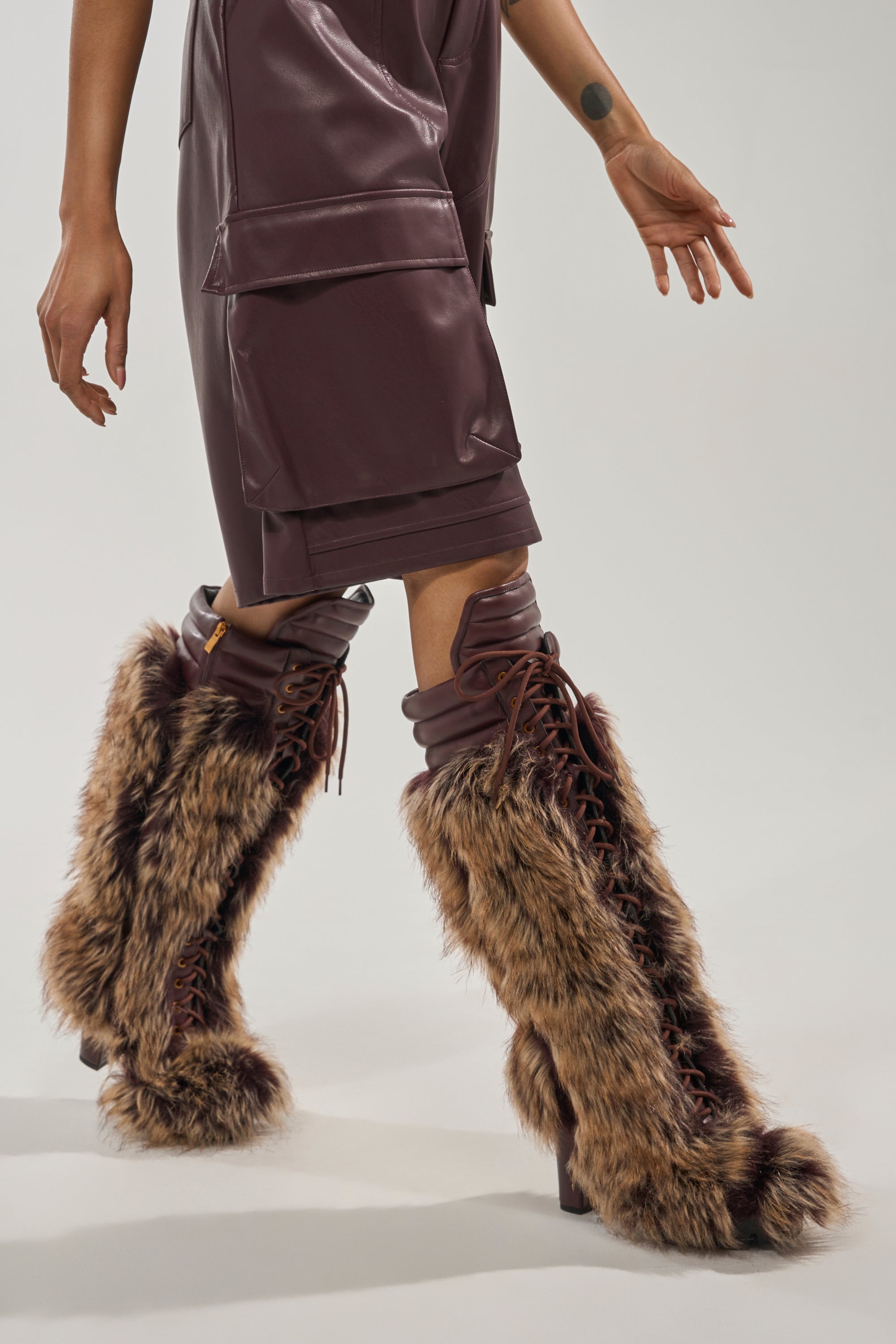 A person in a burgundy faux leather outfit showcases the AZALEA WANG HEARTBEAT BROWN MULTI BLOCK FUR BOOT against a plain light background, with only the lower half visible to highlight these stylish winter boots. 1