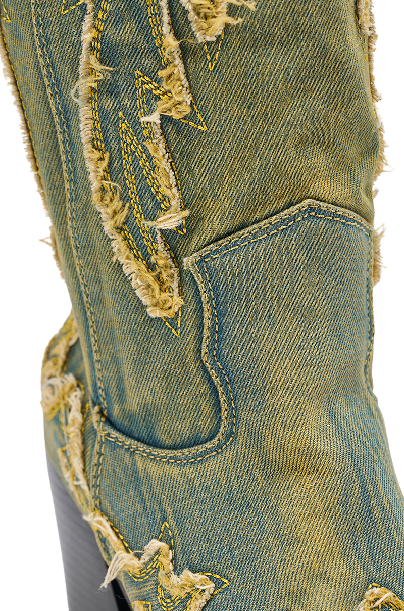 Close-up of the AZALEA WANG HEINRICH DENIM WESTERN LOW HEEL BOOT, featuring yellow stitching, frayed distressed edges, and a detailed denim texture with a low heel design.