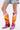 A person in frayed light blue denim shorts and the AZALEA WANG SPICE IT UP CHUNKY BOOT IN MULTI, featuring a faux leather upper with metallic magenta designs, stands against a plain white background.