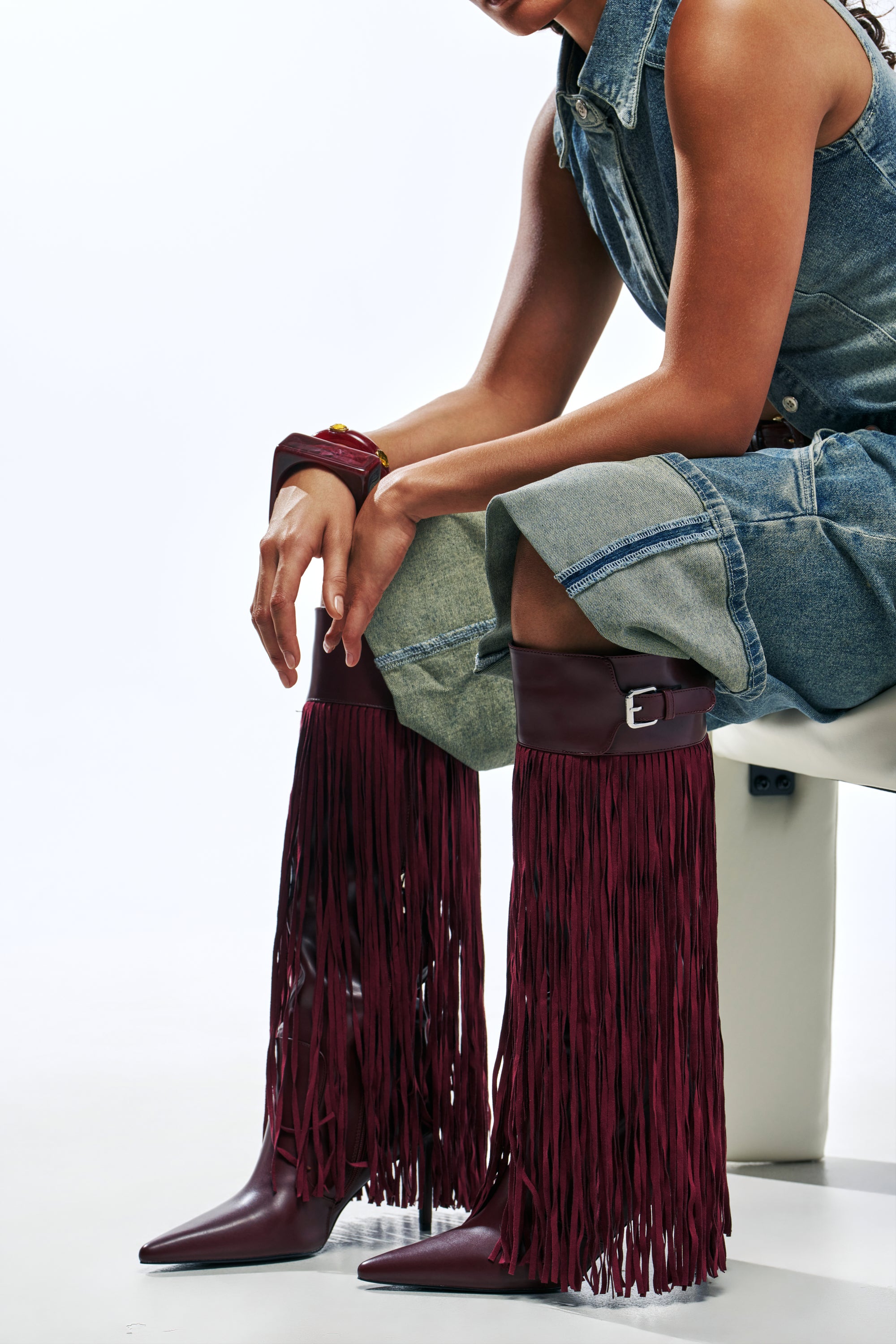 AZALEA WANG HEARTBEAT BURGUNDY FRINGE BOOTs featuring a top buckle strap, worn by a person sitting in denim shorts.