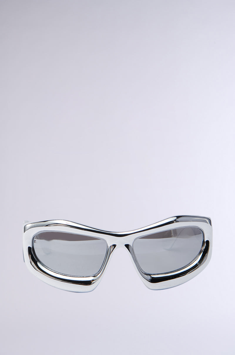 The MOD SH* SUNGLASSES feature a futuristic silhouette with thick frames and grey-tinted rectangular lenses, set against a minimalist light grey background.