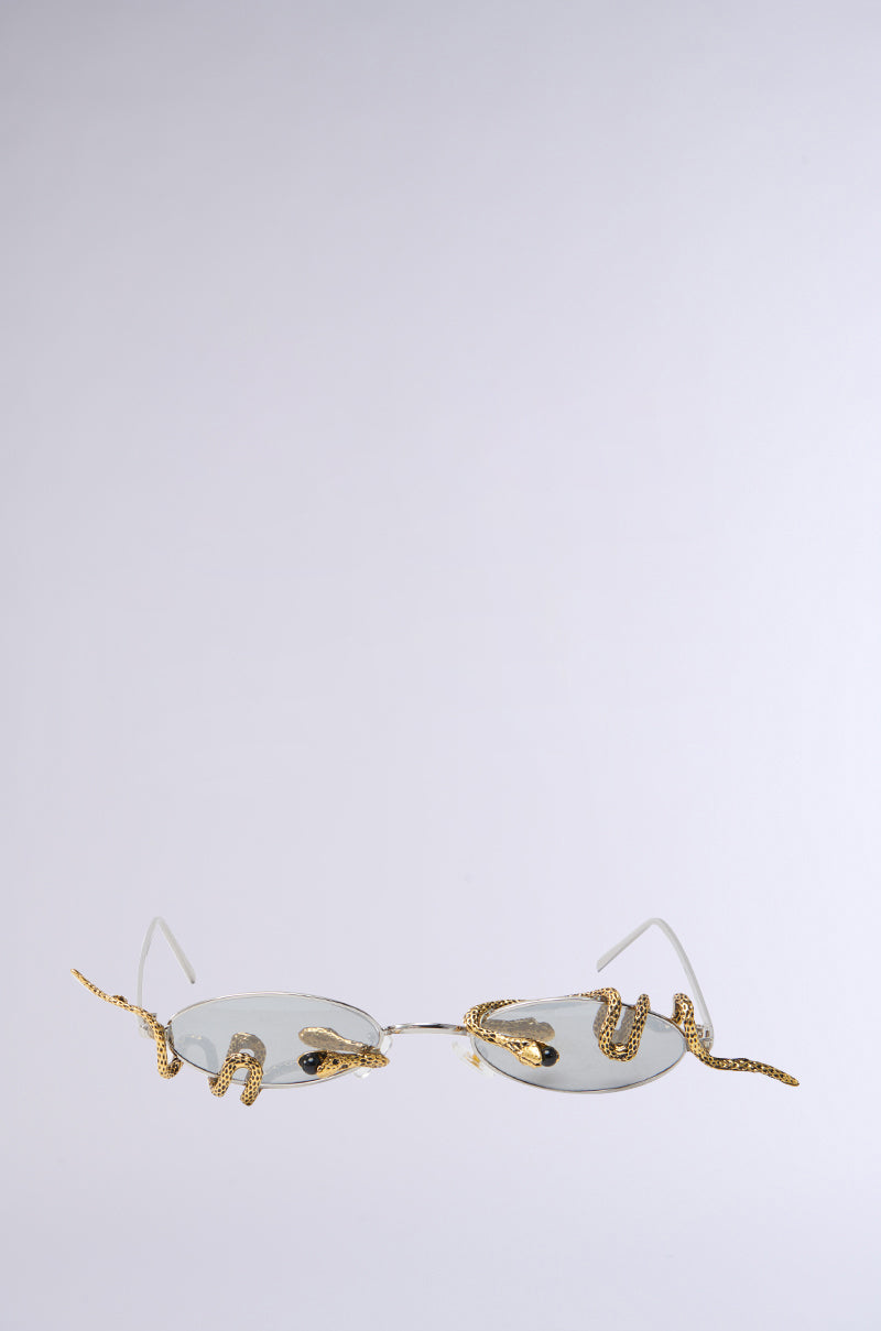 The DONT BE A SNAKE SUNGLASSES boast gold-rimmed, reflective oval lenses with intricate snake designs elegantly winding around the frames, set against a plain backdrop.