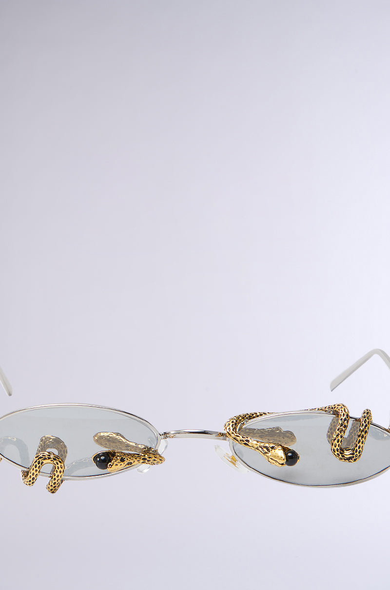 DONT BE A SNAKE SUNGLASSES showcase oval frames with reflective lenses and gold metallic snake embellishments, elegantly set against a simple backdrop.