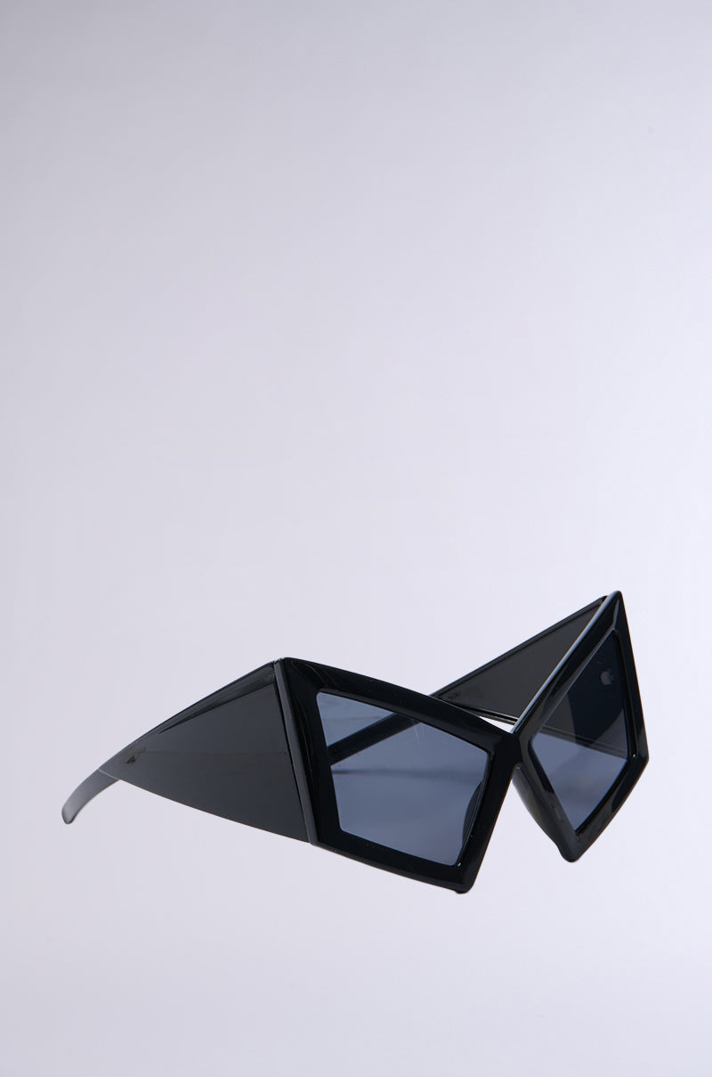 Captured against a plain white background, the U HAVE TO GET IT SUNGLASSES showcase an angular, geometric design with tinted lenses, sharp angles, oversized temple arms, and thick frames in a bold black Matrix-chic style.