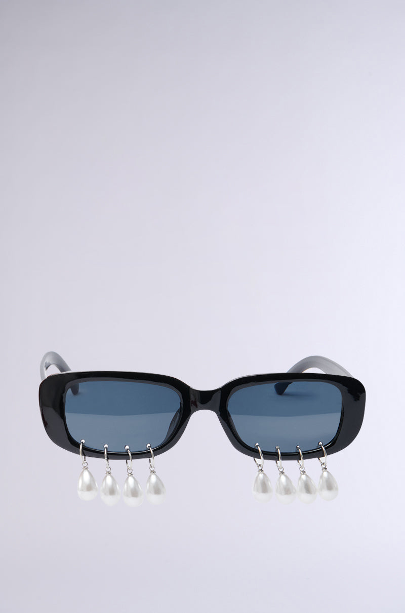 Meet the PEARL PLZ SUNGLASSES: sleek black frames with tinted rectangular lenses and five dangling teardrop pearl embellishments. They stand out against a plain light gray backdrop, making them a true statement piece.