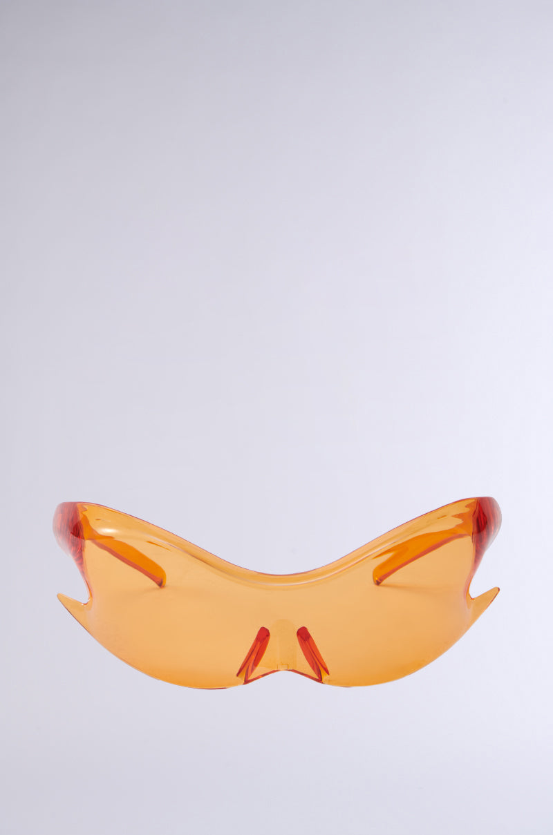 The IM SO FLAME SUNGLASSES flaunt a minimalist design with striking orange, abstractly shaped frames and orange tinted lenses, set against a light gray background.
