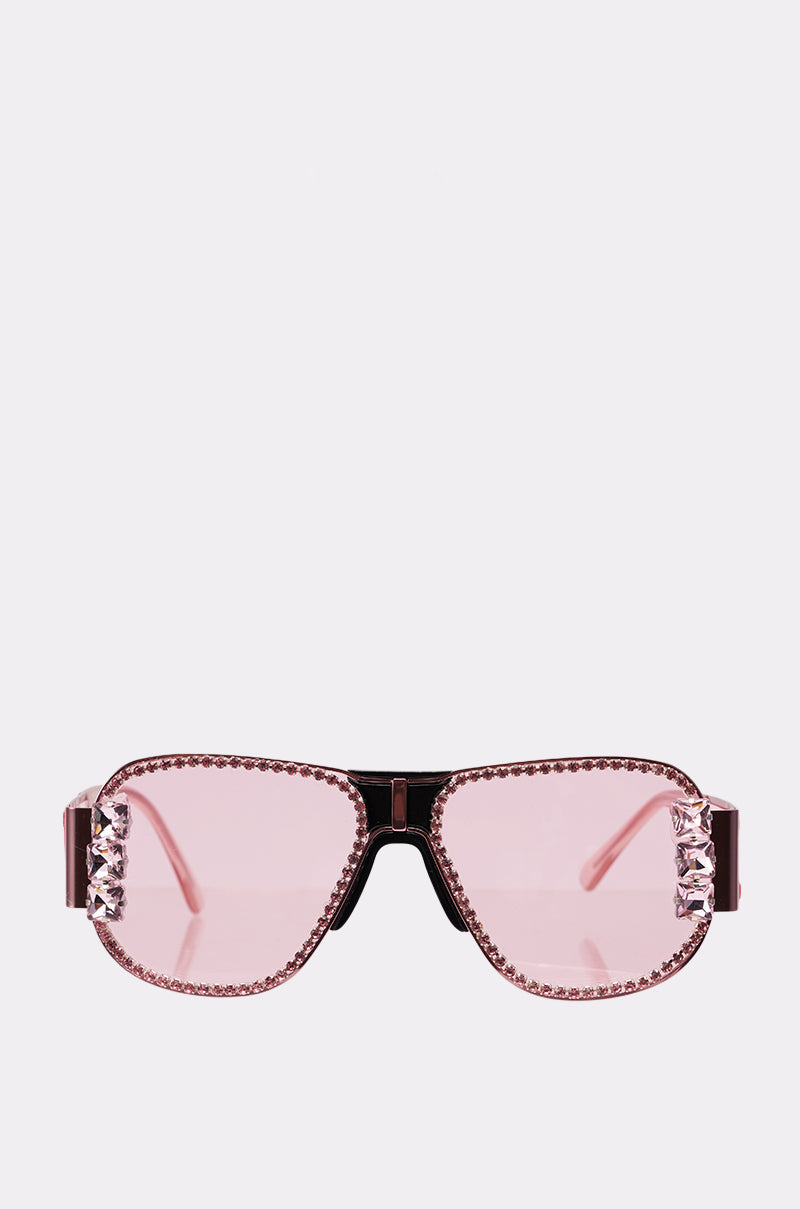 PRETTY IN PINK SUNGLASSES feature large, rectangular lenses accented with pink rhinestones on the edges and temples, adding a glamorous touch to classic sunglasses. Displayed against a plain white background. 0