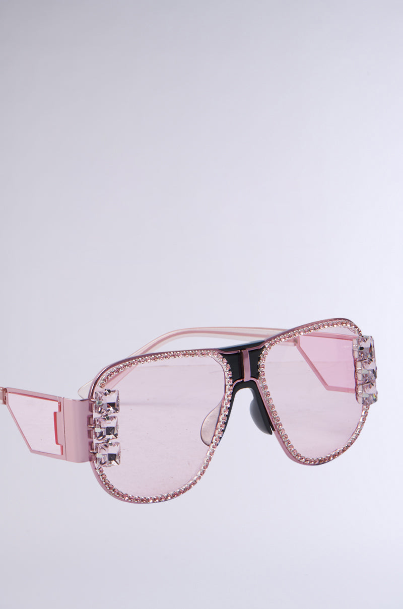 PRETTY IN PINK SUNGLASSES feature rhinestone-trimmed aviator-style frames and temples on a light gray backdrop, with pink-tinted lenses for a bold, fashion-forward look.