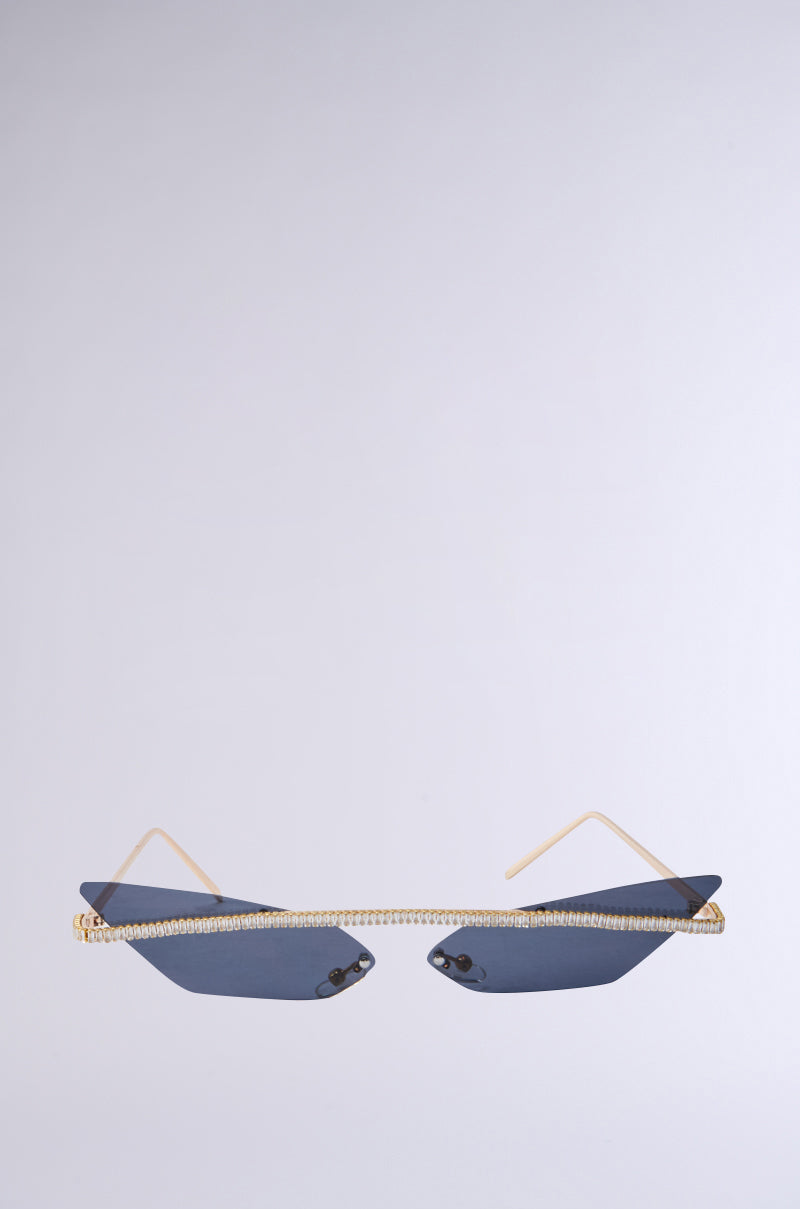 The GET ALIGNED SUNGLASSES feature sleek, angular cat eye frames with dark tinted lenses and thin gold arms. A decorative shiny bridge connects the geometric lenses, all set against a plain, light gray background. 1