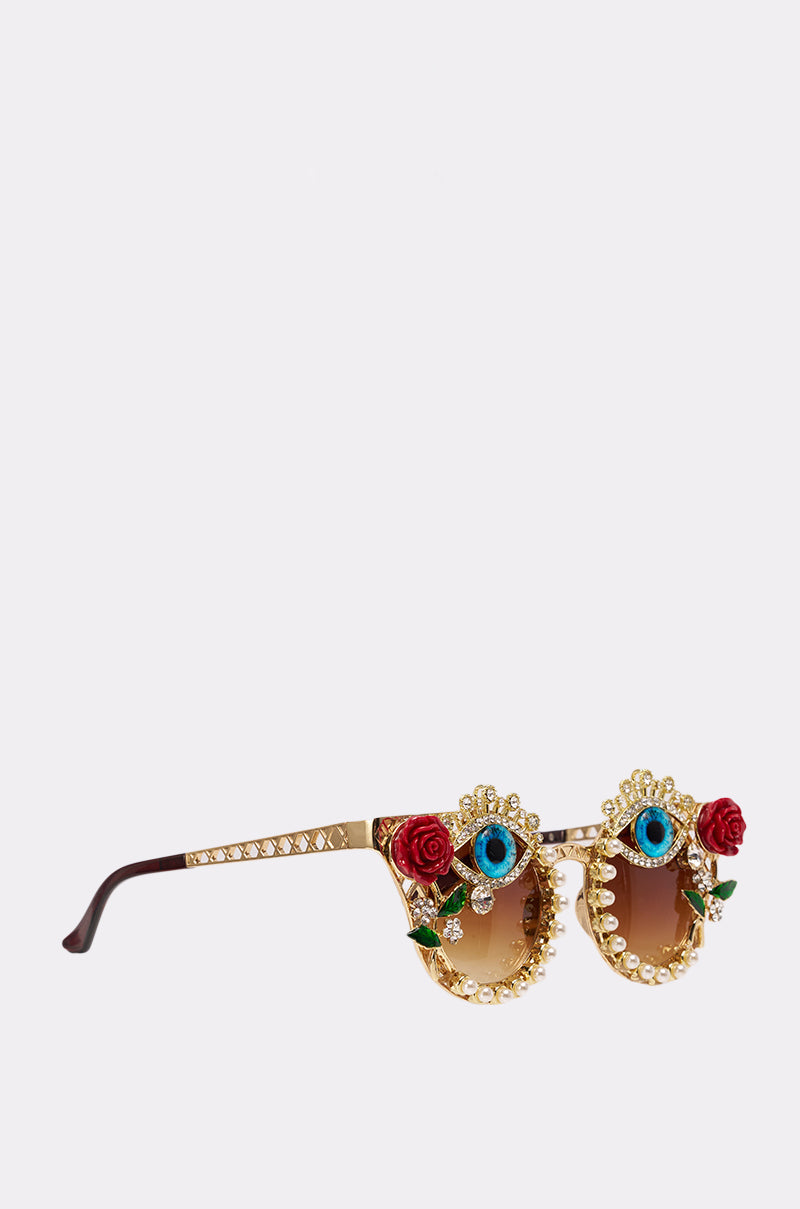 OFF THE RUNWAY SUNGLASSES feature a gold frame adorned with pearls, red roses, blue gemstones, and green leaves on the lenses—perfect for making a bold statement against a plain light background. 2