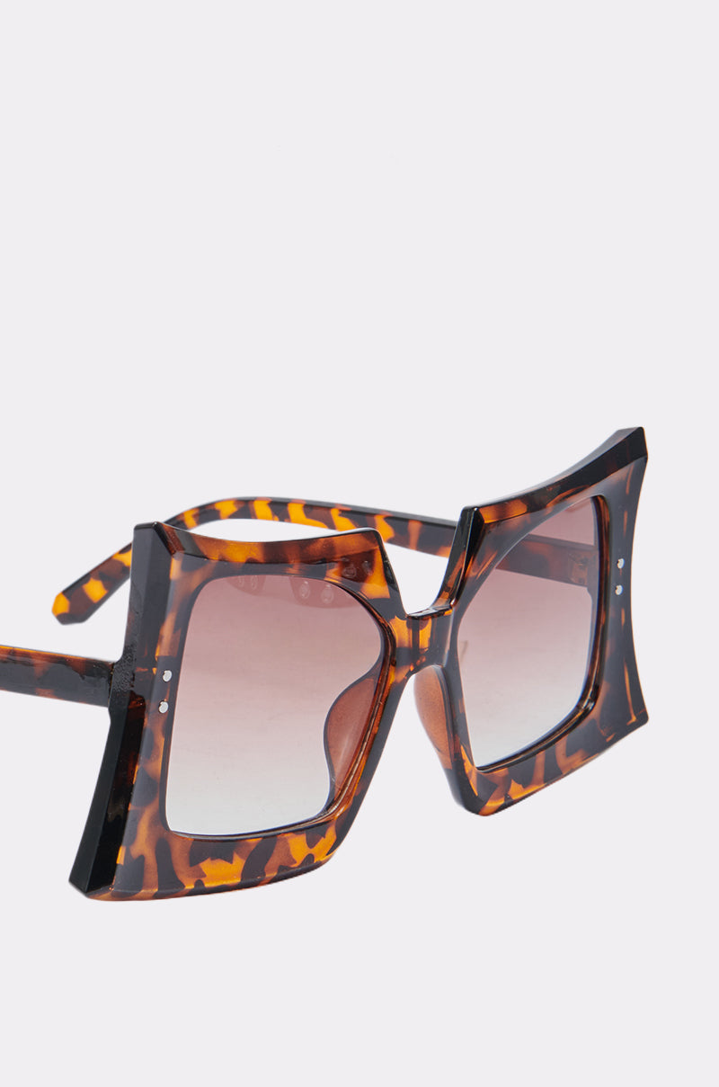 The SHELLY SUNGLASSES feature an oversized square design with a tortoiseshell pattern frame and brown gradient lenses, set against a light background for a retro chic look. 5