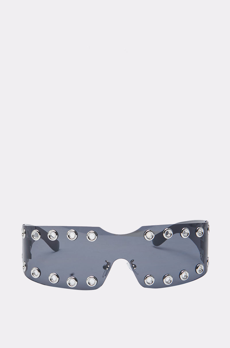 The HERE FOR THE VIBES SUNGLASSES feature a futuristic, oversized wraparound shield design with dark-tinted lenses and silver metal grommet accents along the frame's top and bottom edges. 3