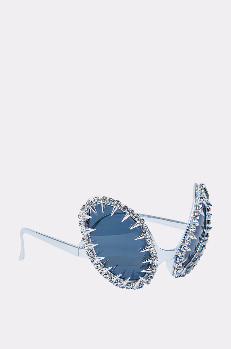 BUGGIN BLING SUNGLASSES: Blue oversized, oval bug-eye frames with zigzag silver edging and a rhinestone border on each lens, shown on a plain white background.